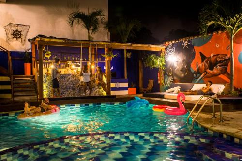 Photo of a pool at a best hostel in Cartagena at night with a guy on a float in the corner of hte pool, some people at a bar behind the pool, and a mural on the wall