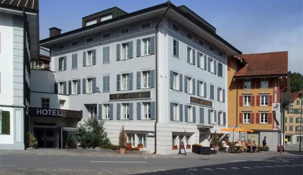 Hotel Metzern with blue shutters and potted plants on a cobblestone square with outdoor café and yellow-red building at Hotel Metzgern in Sarnen
