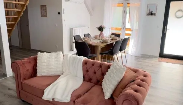 Open-plan living area with pink tufted sofa, round coffee table, dining table with chairs and sunlit balcony doors at Gîte duplex les Glycines in Bennwihr