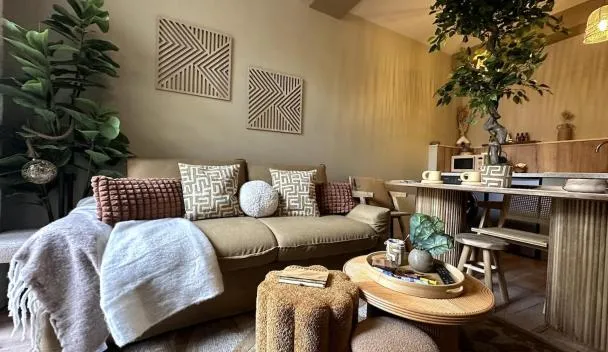 Living area with beige sofa, patterned pillows, geometric wall art, rattan coffee table, woven stool and desk with plant at LE COTTAGE, T2, Hyper center, Terrasse in Mâcon