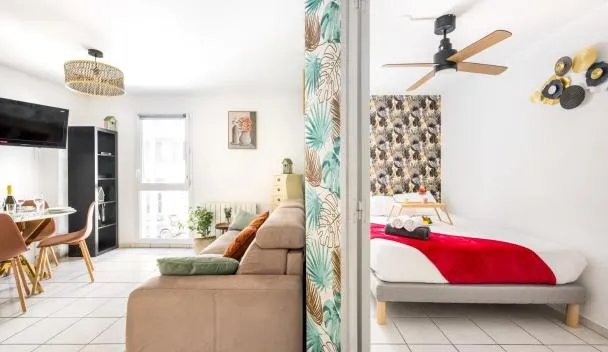 Open-plan studio with sofa, dining table, wall TV, patterned accent wall and bed with red throw and rolled towels at BnGo l Cosy et Calme l Métro B, 4 personnes in Lyon