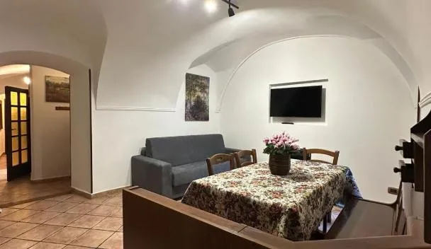Vaulted white-arched living/dining area with sofa, wall-mounted TV, dining table with vase and terracotta tile floor at Il Dolce Rustico in Dolceacqua