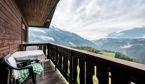 Wooden balcony with table and chairs overlooking green valley, mountain ridges and low-lying fog under cloudy sky at Ferienwohnung Gatscherhof in Luson