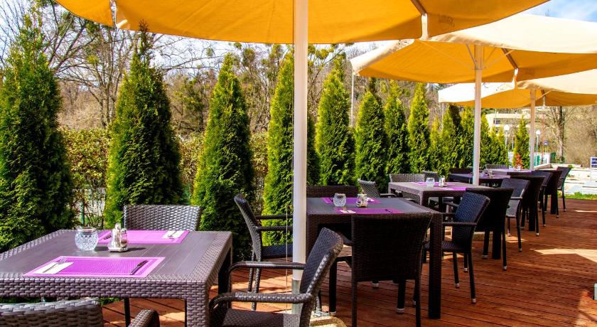 a patio area with tables, chairs and umbrellas, Hotel Aurora in Miskolc