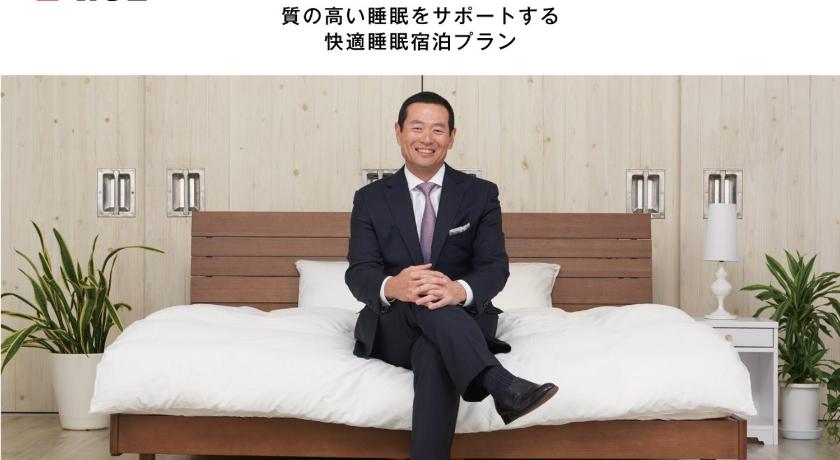 a man in a suit and tie sitting on a bed, Value The Hotel Ishinomaki in Ishinomaki