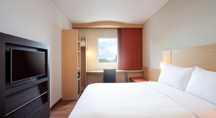 a hotel room with a bed, tv and a desk, Ibis Makassar City Center Hotel in Makassar
