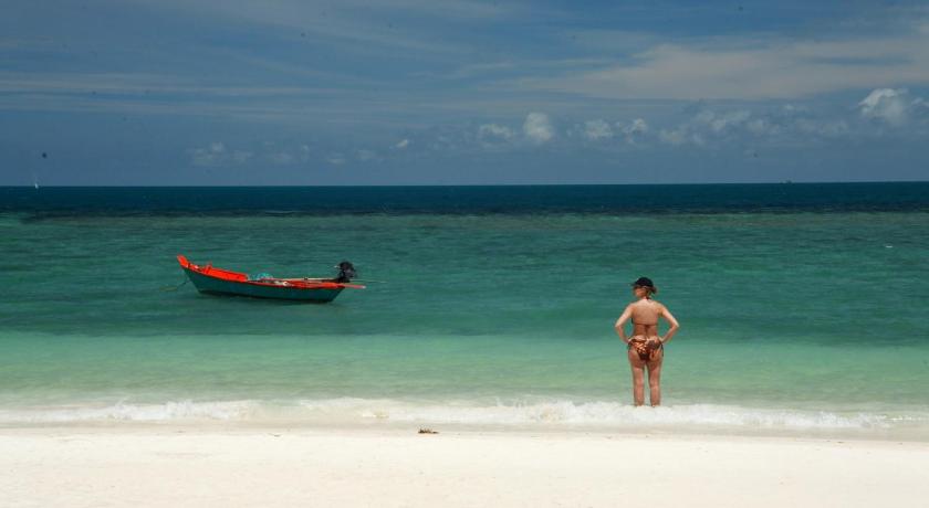 a man standing on a beach next to a boat, See Through Boutique Resort in Ko Pha-ngan