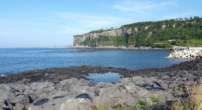 a rocky shoreline with rocks and a lighthouse, Soo Pension in Jeju
