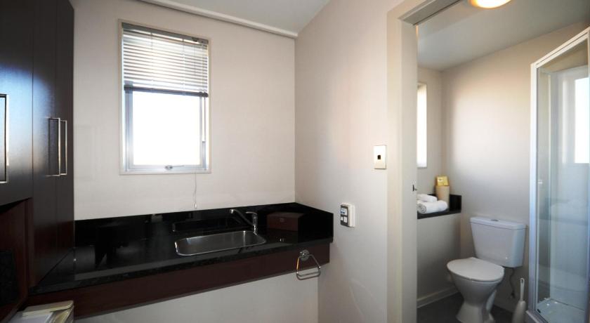 a white toilet sitting under a window in a bathroom, City Central Motel Apartments in Christchurch
