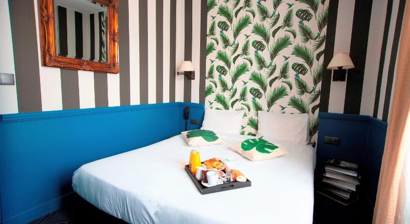 a bed with a blue comforter next to a window, Hotel du Theatre in Paris