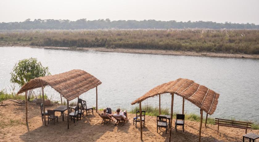 people sitting at a picnic table in front of a body of water, Jungle Wildlife Camp in Chitwan