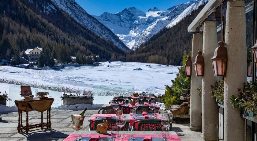 a row of red and white tables and chairs in front of a mountain range, Bellevue Hotel & SPA in Cogne