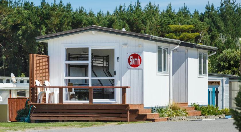 a white house with a red door and a white fence, Foxton Beach Holiday Park in Foxton Beach