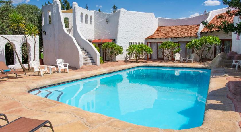 a white swimming pool with a blue couch and chairs, By Bush Telegraph Lodge in Johannesburg