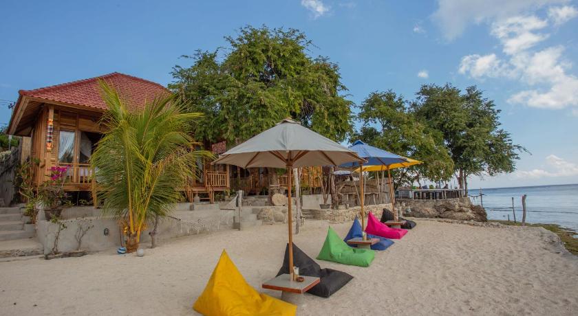 a beach area with a beach umbrella and chairs, Wooden Beach Sunset Cottages in Bali