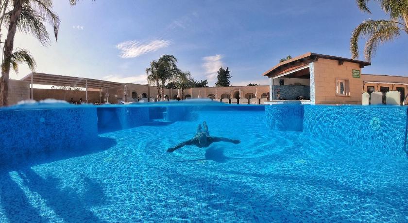a man is swimming in a pool in front of a building, La Pineta Residence in Otranto
