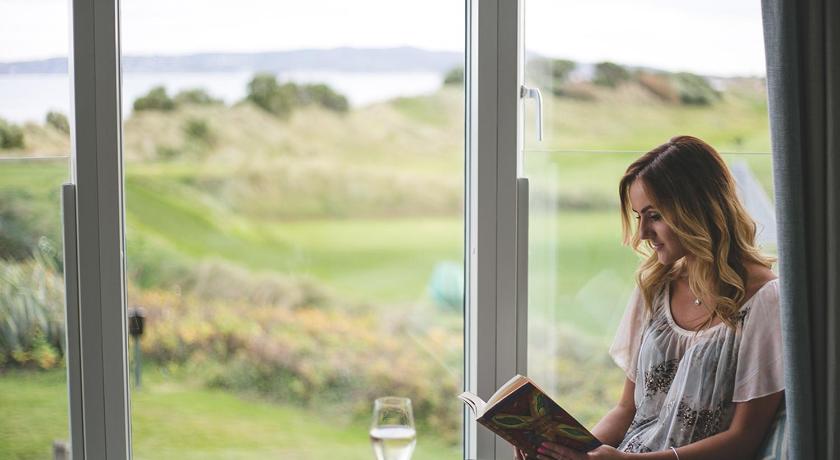 a woman sitting at a table reading a book, Portmarnock Hotel & Golf Links in Dublin