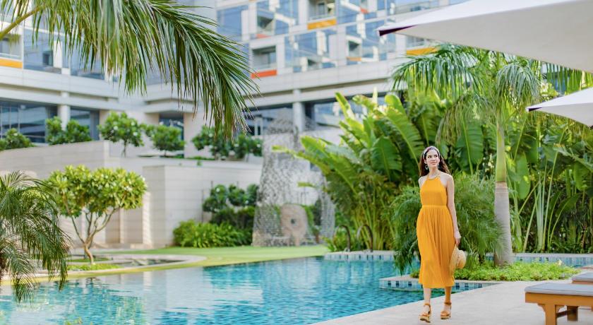 a woman standing in front of a pool holding an umbrella, Andaz Delhi – A Concept By Hyatt in New Delhi and NCR