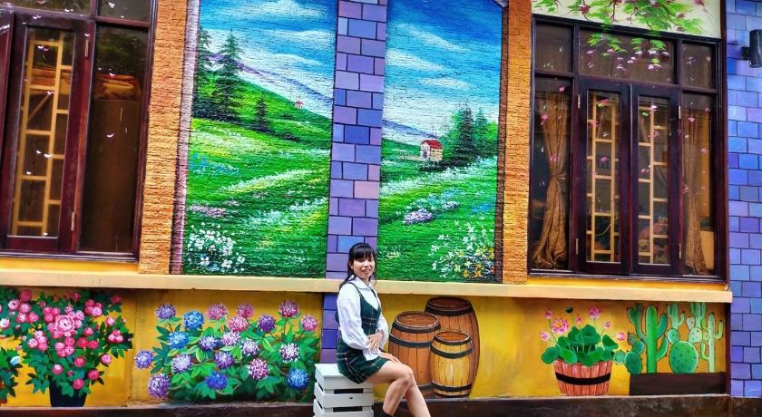 a woman sitting on a bench in front of a mural, An Nhien Hotel. in Buon Ma Thuot