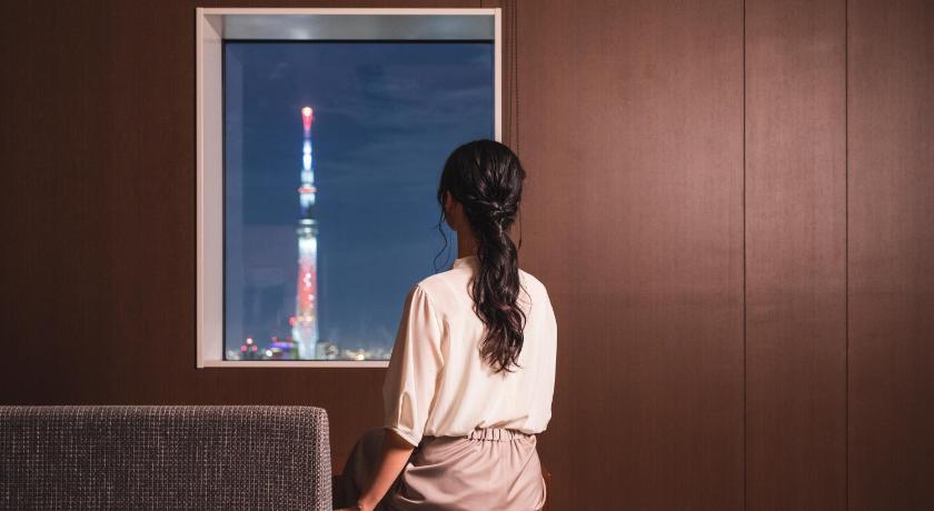 a woman sitting on a bench looking at a television screen, Hotel Crown Hills Ueno Premier in Tokyo