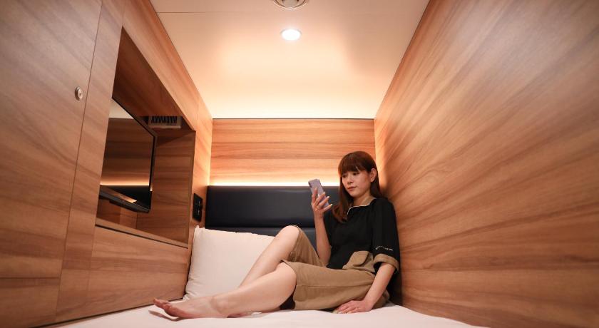 a man sitting on a bed talking on a cell phone, Smart Stay SHIZUKU Shinagawa-Oimachi in Tokyo