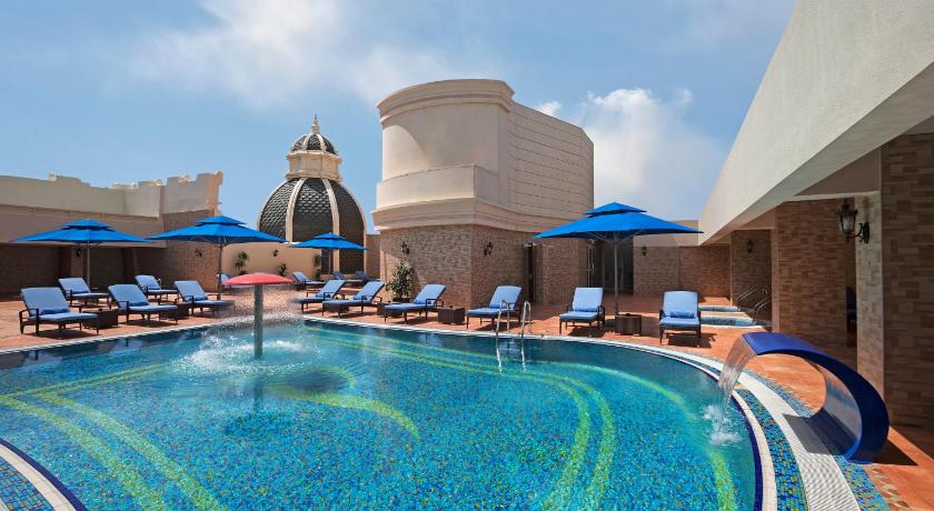 a swimming pool with blue chairs and blue umbrellas, Royal Rose Hotel in Abu Dhabi