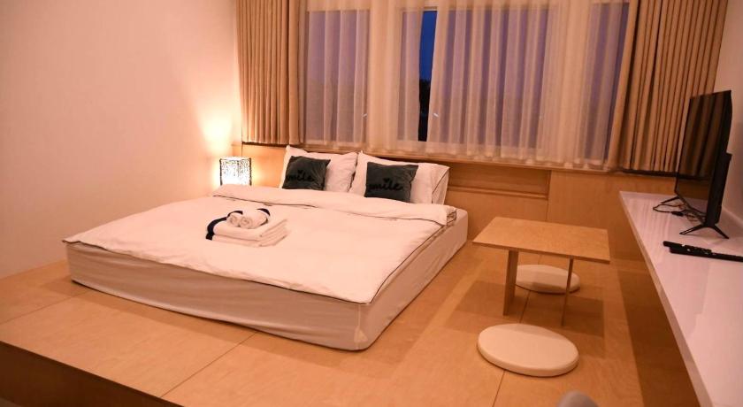a hotel room with a white bed and white walls, Ma-TaO またお Cafe & hostel in Nan