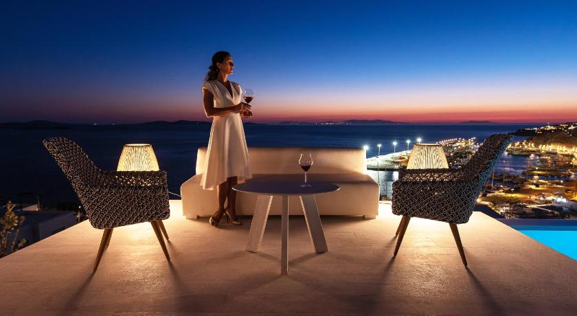 a woman standing on a balcony overlooking a beach, Mykonos Riviera - Small Luxury Hotels of the World in Mykonos