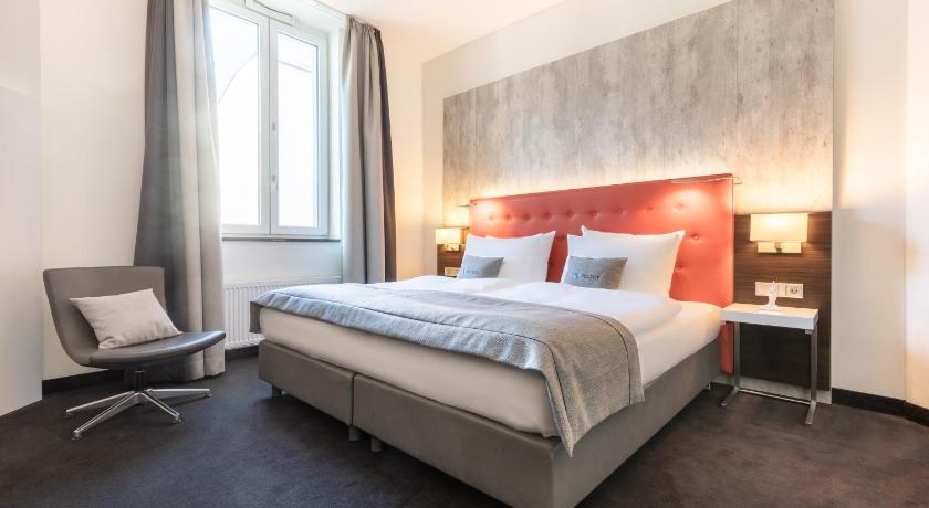 a hotel room with a bed, chair, and nightstand, Select Hotel Berlin The Wall in Berlin