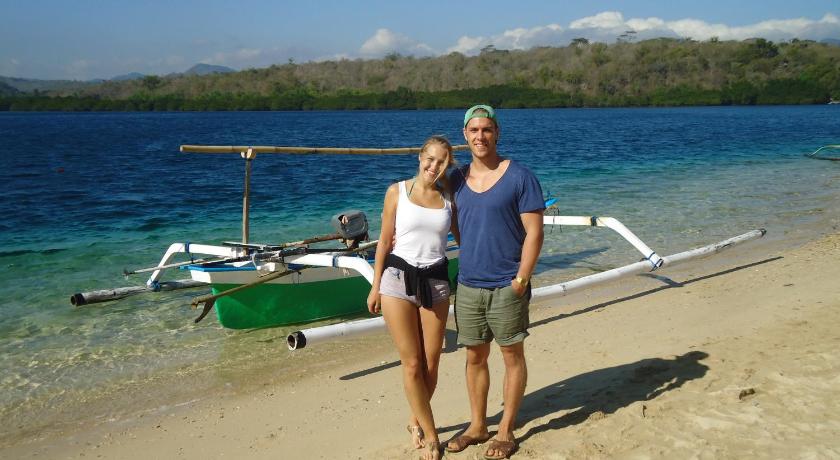a man and a woman standing on a beach with a surfboard, Made Taro - Menjangan Homestay in Bali