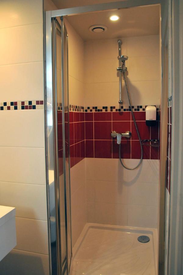 White-tiled shower with red accent tiles and chrome fixtures stands at pet-friendly Hôtel Des Quatrans in Caen.