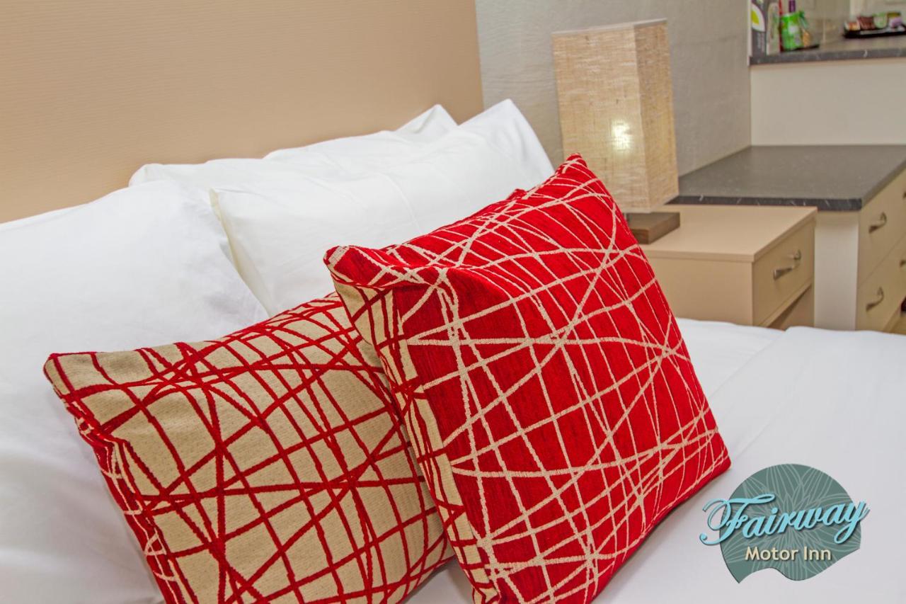 Two red and beige patterned pillows rest on white bed at dog-friendly Fairway Motor Inn in Pambula.