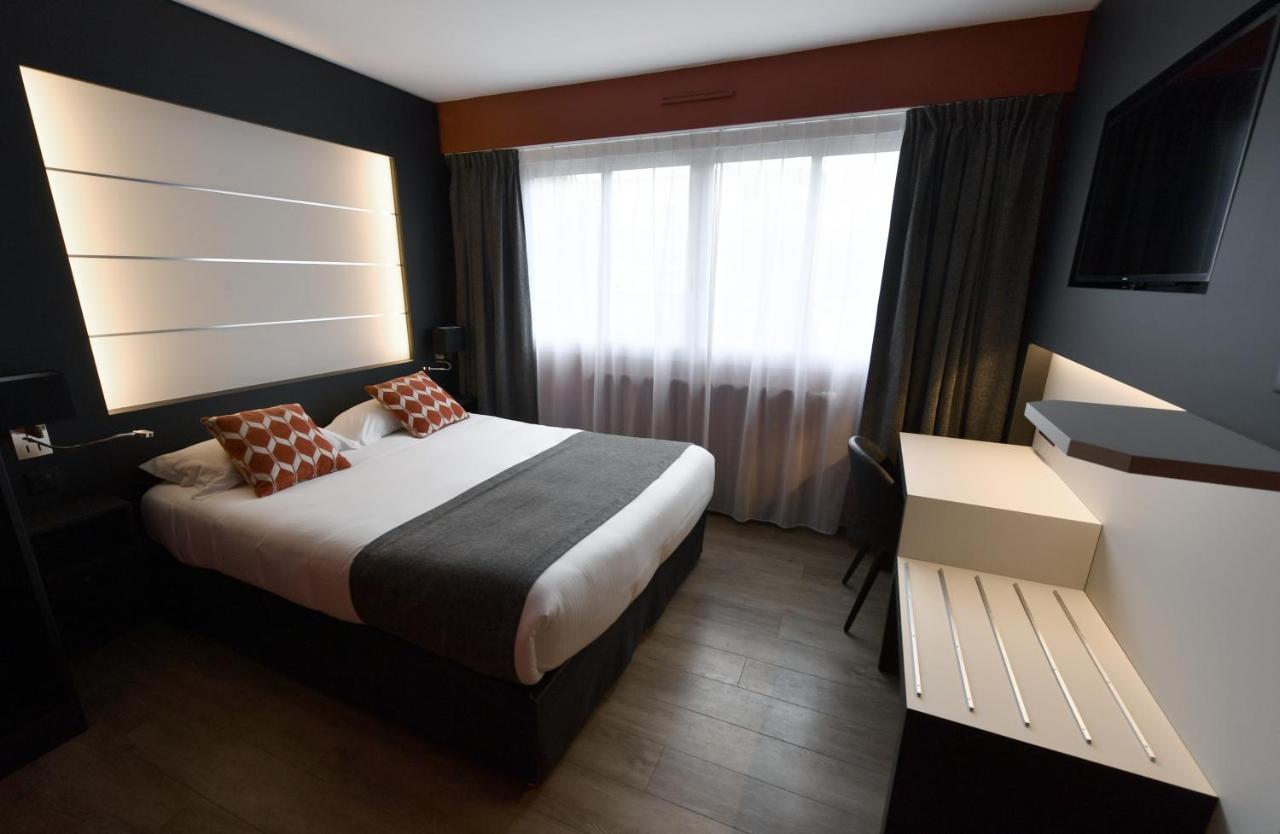Double bed with white sheets and gray runner sits at dog-friendly Hôtel Des Quatrans in Caen.