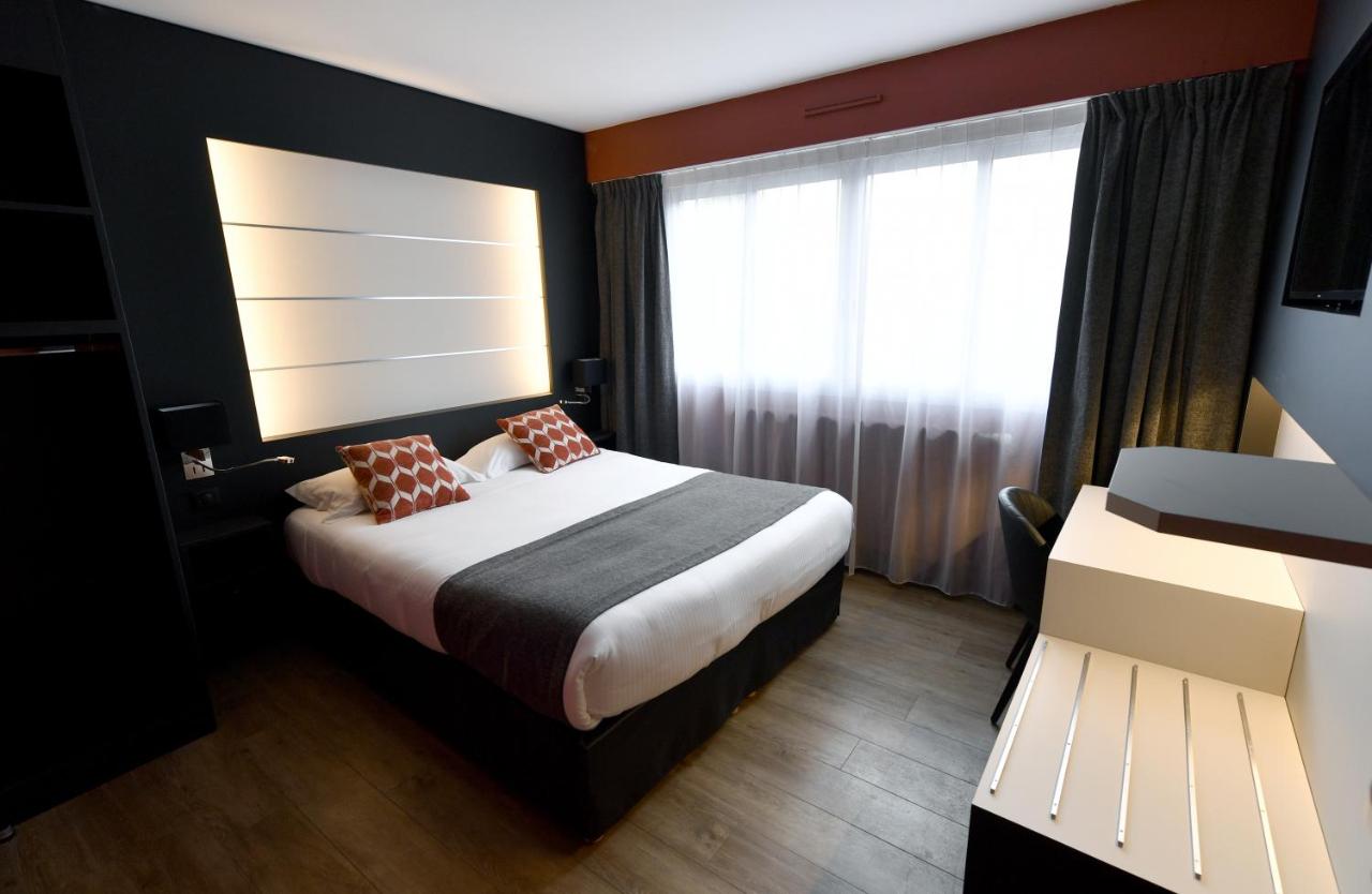 White bed with gray runner and orange patterned pillows sits at dog-friendly Hôtel Des Quatrans in Caen.