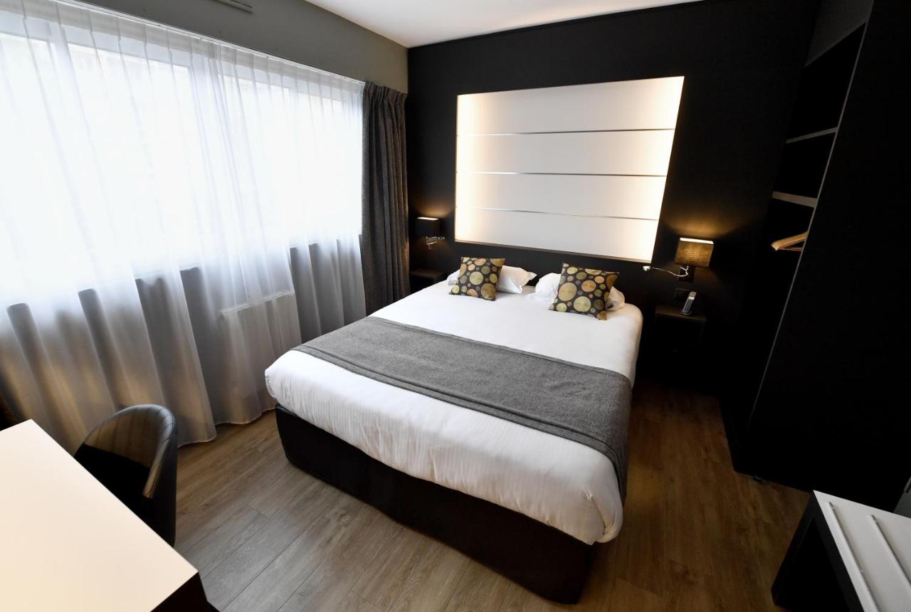 White bed with gray throw and two patterned pillows sits at dog-friendly Hôtel Des Quatrans in Caen.