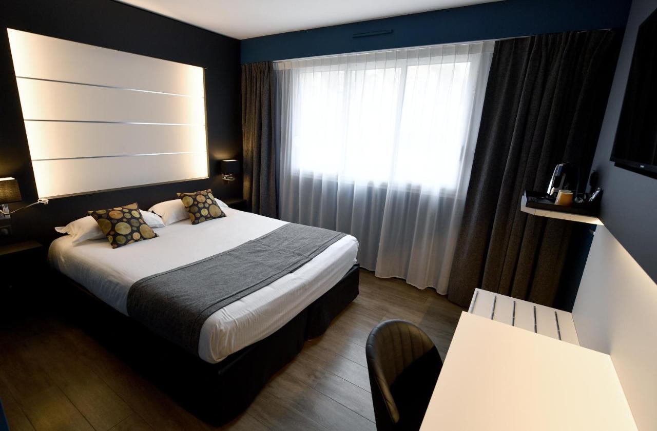 White bed with gray throw and patterned pillows sits at dog-friendly Hôtel Des Quatrans in Caen.
