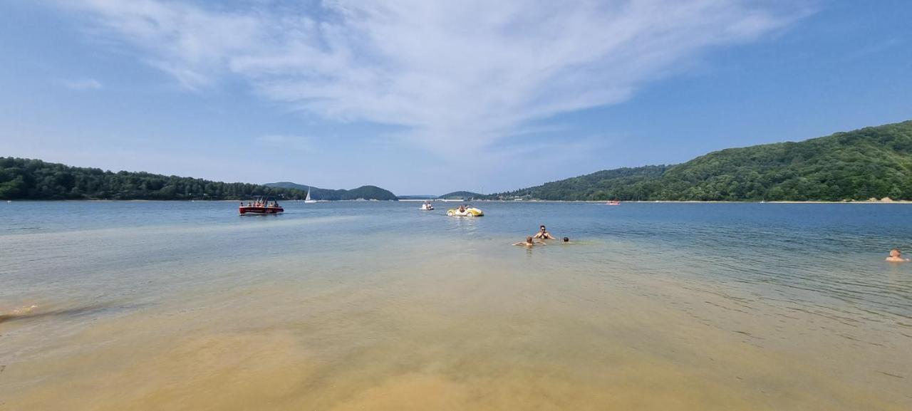 Man in black swim trunks and sunglasses wading at dog-friendly Domki Z Klimatyzacj W Centrum Soliny - Pokoje Z Balkonami SPA - B&B Zadzwo I Zapytaj O Biece Zniki - 695-744-679 in Solina.