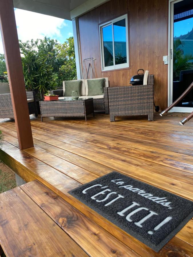 Brown wicker sofa with green cushions sits on wooden deck at dog-friendly Fare Maraea in Vaiare.