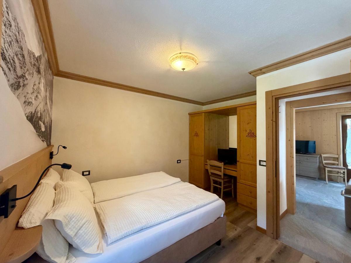 Bed with white bedding and wooden headboard sits near doorway at dog-friendly Rosengarden Alpine Residence in Valdidentro.
