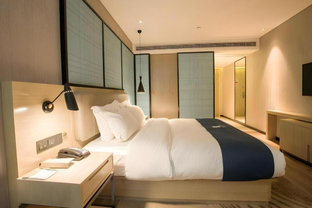 A white bed with navy runner sits at dog-friendly Echarm Hotel Wuhan Plaza Wansongyuan in Wuhan.
