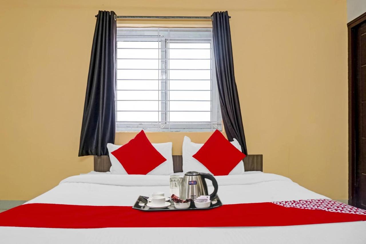 Bed with red pillows and kettle sits by window at pet-friendly Hotel O Sapphire Homes Stay in Hinjawadi.