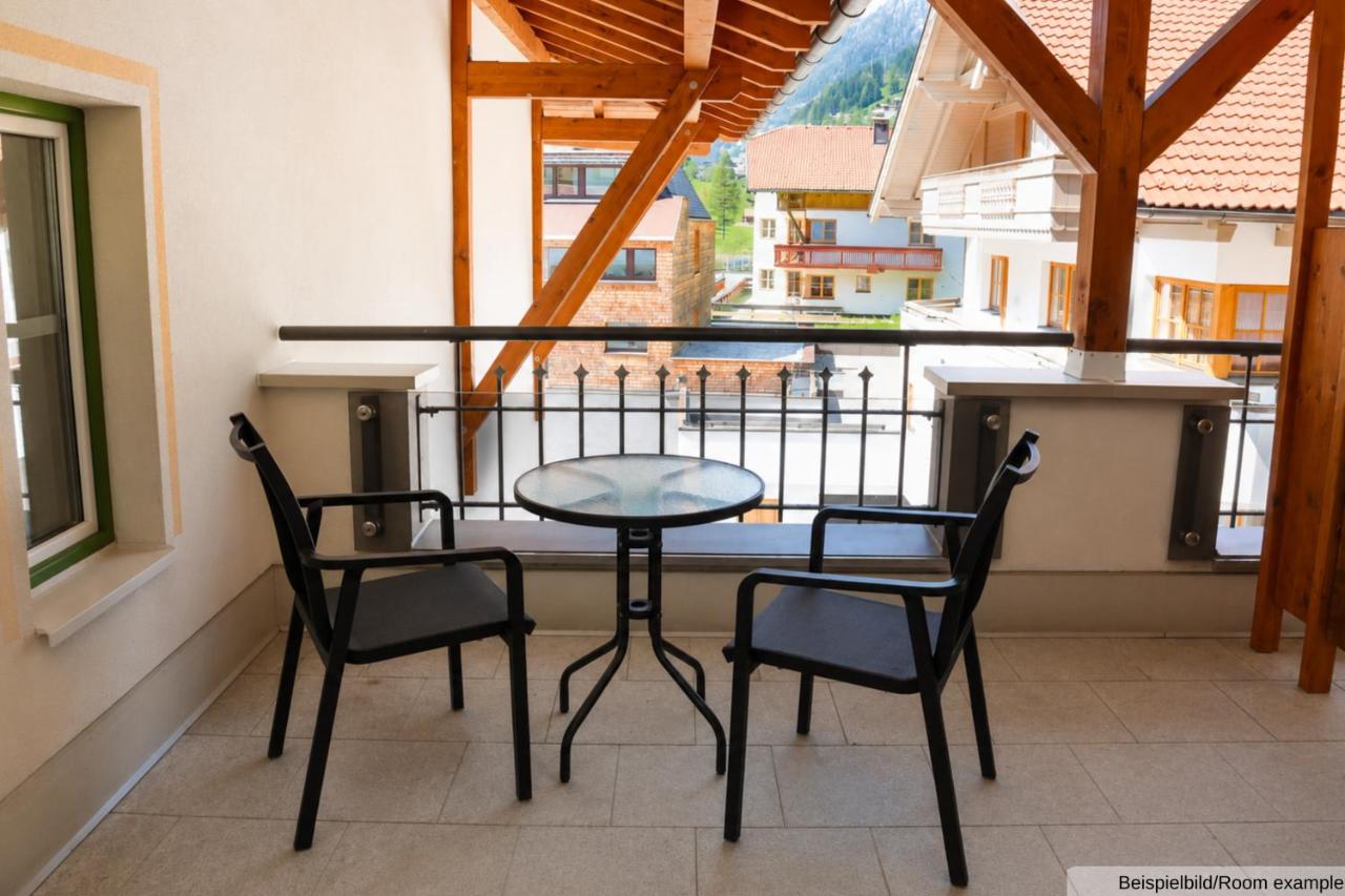 Two black metal chairs and round glass table sit on tiled balcony at dog-friendly Sporthotel Auhof in Kappl.