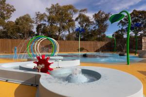 a fountain in a swimming pool with a large swimming pool behind it, Alivio Tourist Park Canberra in Canberra