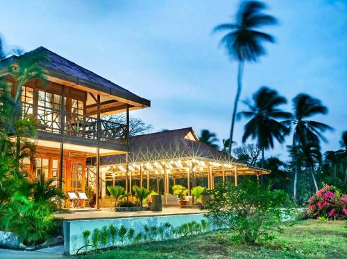 A wooden two story San Andres Island hotel with balconies next to a large wooden covered area lit at dusk with a pool in front