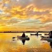 a group of people kayaking on a lake at sunset