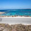 two people riding a bike on a road near the ocean