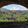 two people sitting in a cave looking at a canyon