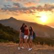 three girls standing on top of a mountain at sunset