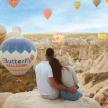 a man and woman sitting on a rock watching hot air balloons