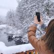 a woman taking a picture of a snow covered lake